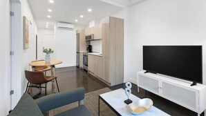Un soggiorno moderno con una TV a schermo piatto, un divano, un tavolino da caffè e un'area pranzo con sedie e un piccolo tavolo.