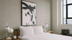 Una camera d'albergo con un letto grande, un comodino con una lampada, un'opera d'arte astratta incorniciata e una finestra vista.
