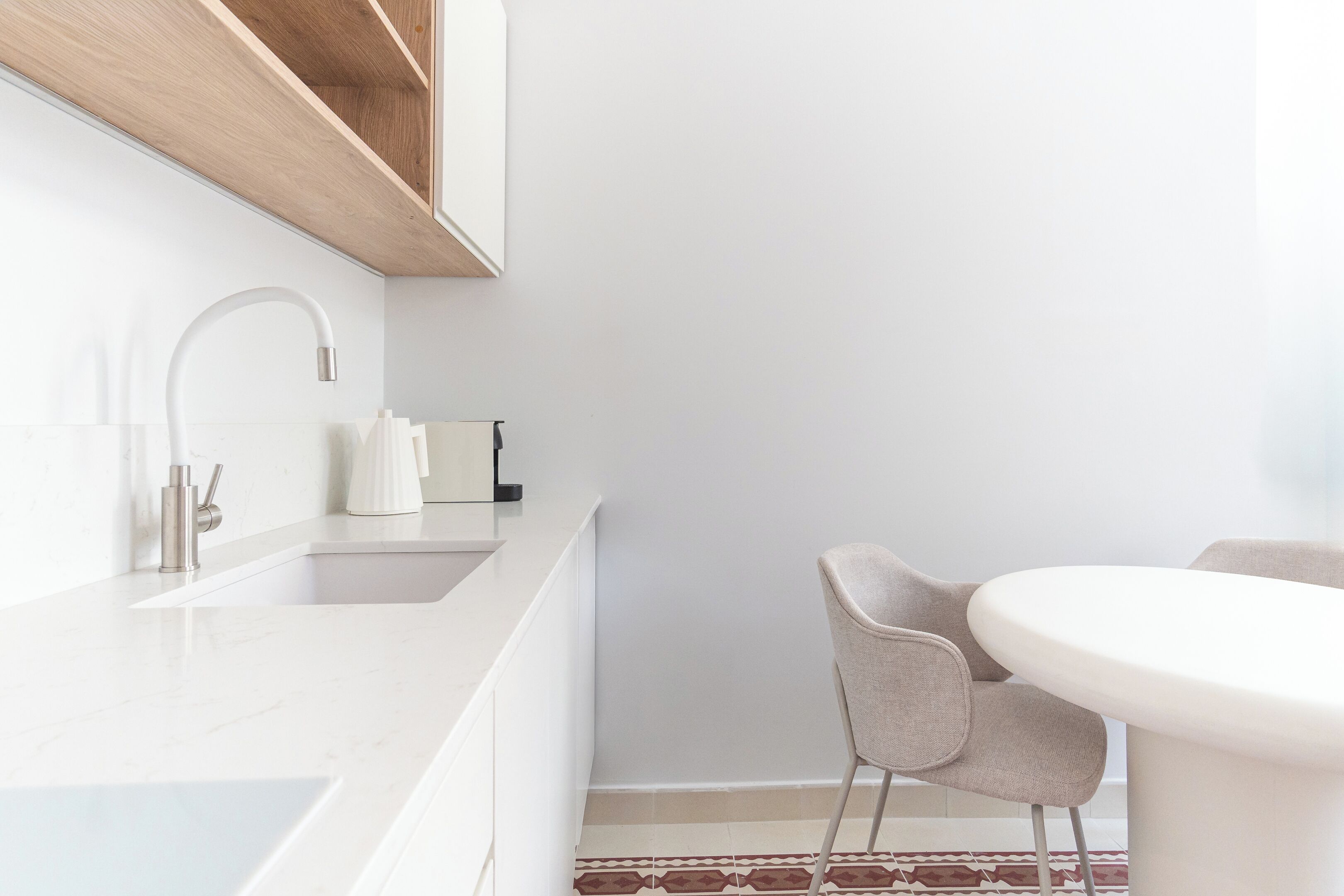 A modern kitchen with a white countertop, a built-in sink, and a round dining table with two chairs.