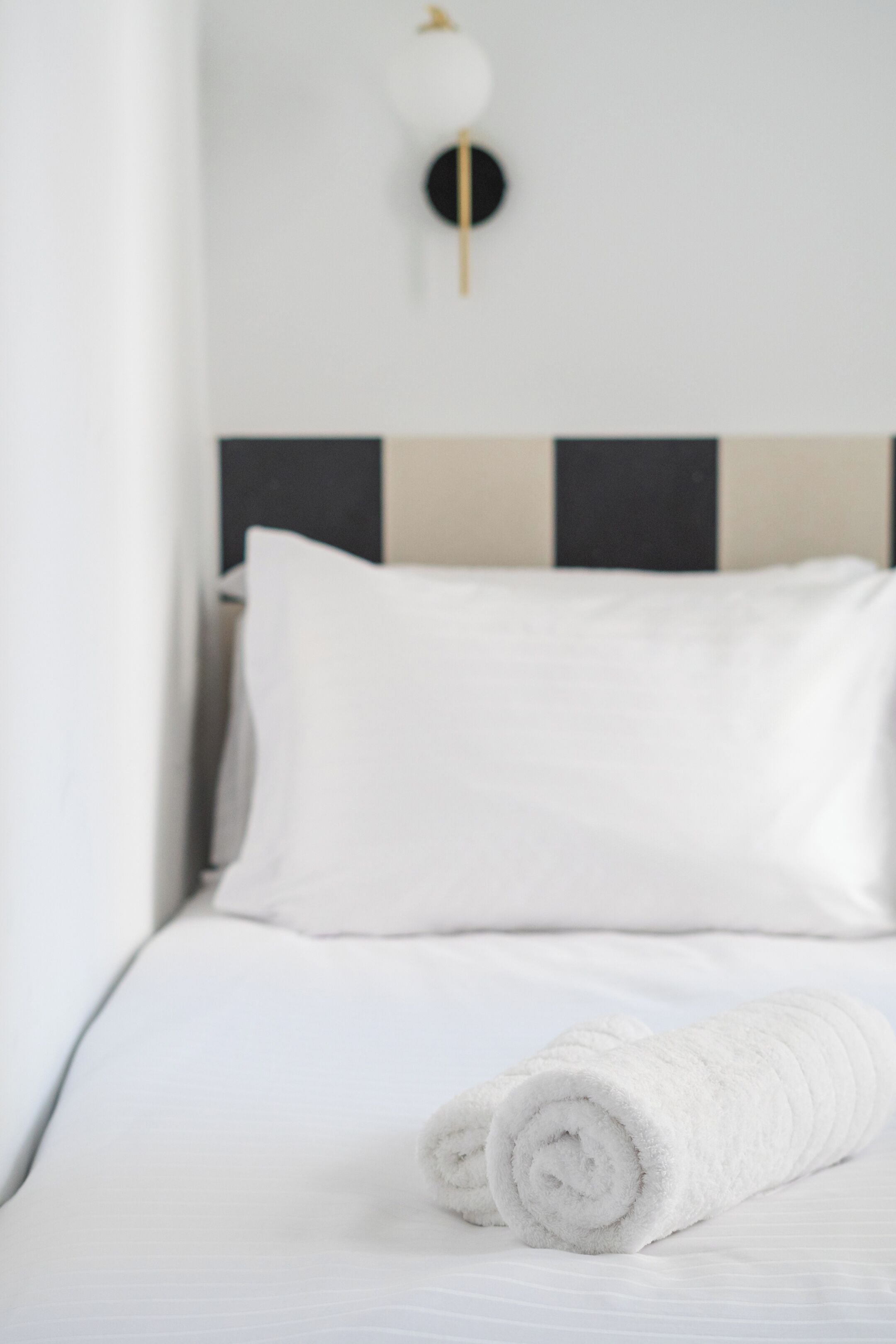 A neatly made bed with white linens and a rolled white towel.