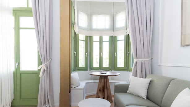 Una habitación con puerta verde, una mesa redonda, un sofá y un ventanal con cortinas.