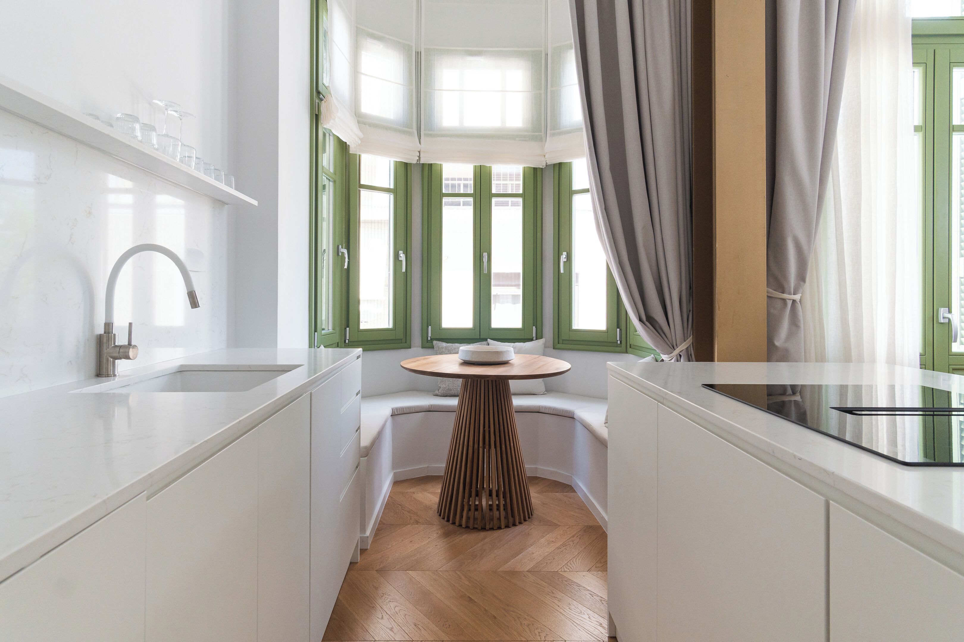 A modern kitchen with a white countertop, a built-in sink, and a round wooden table.