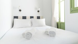 Una cama bien hecha con sábanas blancas y toallas dobladas, un cabecero a rayas y dos lámparas fijadas a la pared.