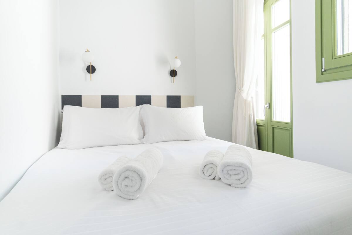A neatly made bed with white linens and rolled towels, a striped headboard, and two wall-mounted light fixtures.