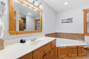 A bathroom with a large mirror, wooden cabinets, a white sink, and a bathtub. - Blue Sky Lodge For 4 (Reeds Spring)