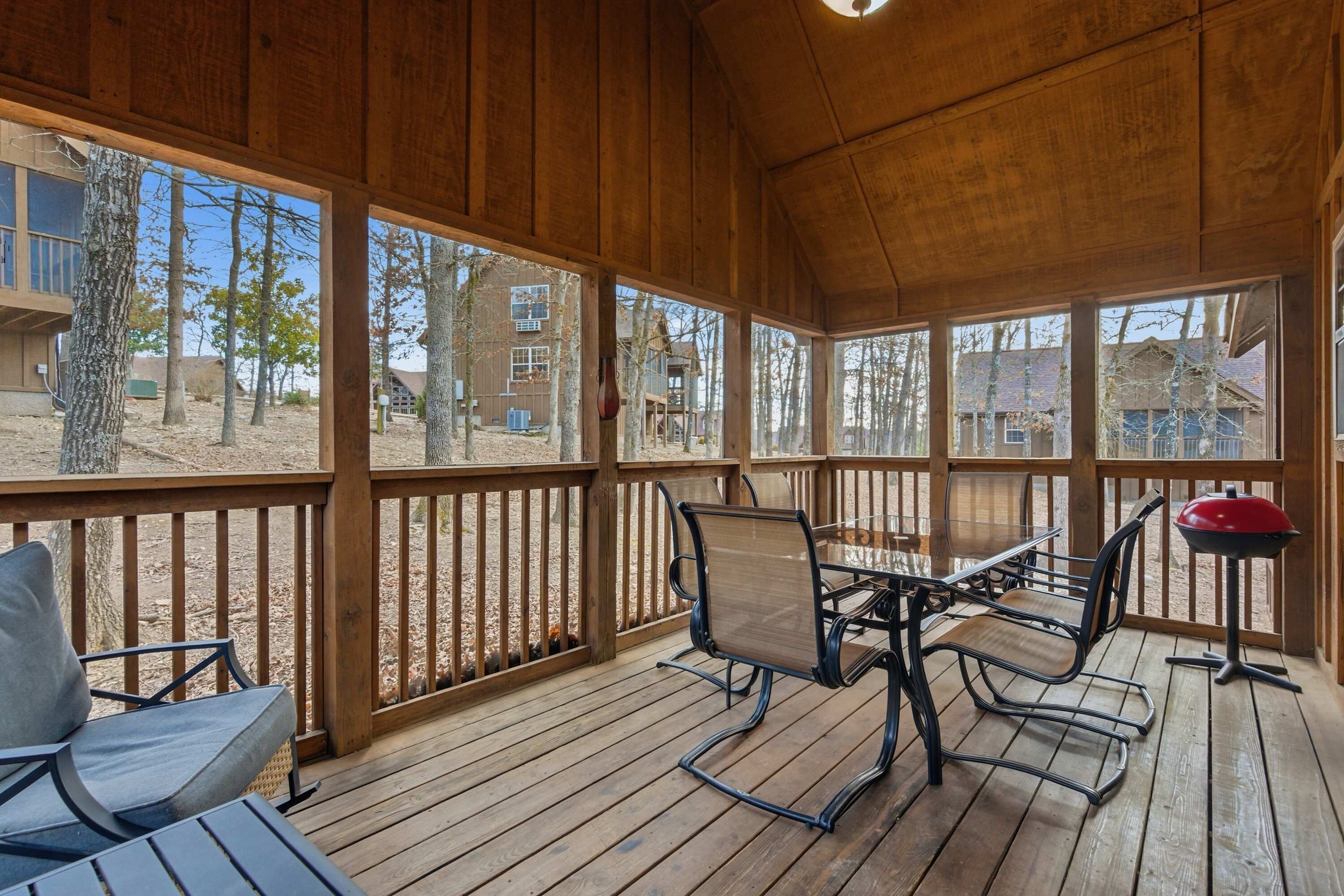 A covered outdoor area with a wooden deck, a table with chairs, and a barbecue grill.