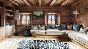 A cozy log cabin interior with a sofa, pillows, a zebra-patterned rug, and a painting on the wall. - Luxury Chalet with Private Sauna and Gym (Cortina d'Ampezzo)