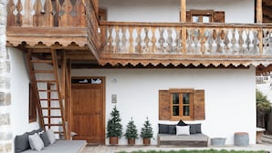 A traditional wooden house with a balcony, a wooden door, a number '78' on the wall, and a small garden area with a bench and potted plants. - Luxury Chalet with Private Sauna and Gym (Cortina d'Ampezzo)