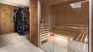 A sauna room with wooden walls and a glass door, a bench, and a sauna machine. - Luxury Chalet with Private Sauna and Gym (Cortina d'Ampezzo)
