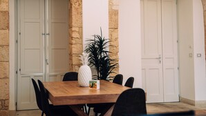 A dining area with a wooden table, black chairs, and a pineapple centerpiece. There are two white doors and a stone wall. - Maison Dumah (Siracusa)