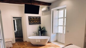 A modern bathroom with a freestanding bathtub, a large mirror, and a potted plant. - Maison Dumah (Siracusa)