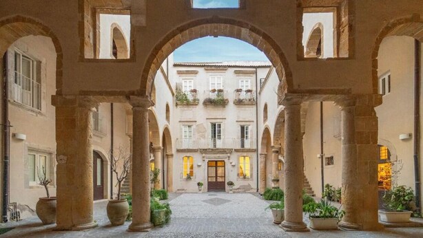 An architectural courtyard with arches, a central door, and potted plants. - Maison Dumah (Siracusa)