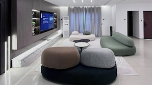 Een moderne woonkamer met een flatscreen televisie, een zithoek en een groot raam met gordijnen.