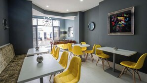 Un espace repas moderne avec des chaises jaunes et des tables blanches, un canapé et une grande fenêtre donnant sur un beau paysage.