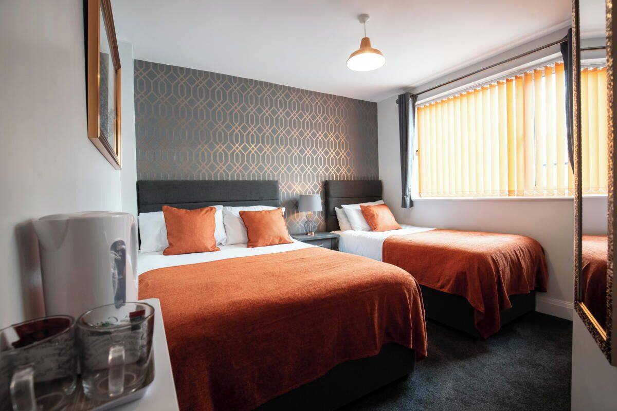 Une chambre d’hôtel avec deux lits, un mur orné de motifs, une grande fenêtre avec des rideaux et un luminaire suspendu.