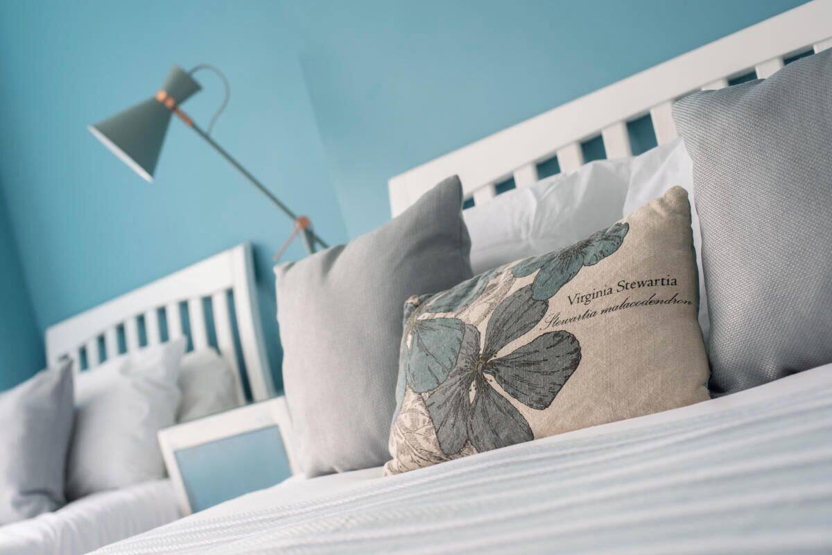 Un lit bien fait, avec une tête de lit blanche, un coussin décoratif à motifs floraux et une lampe de chevet.