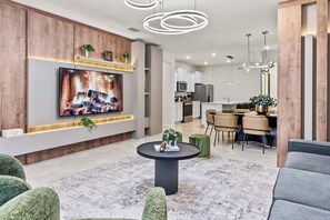 Ein modernes Wohnzimmer mit Flachbildfernseher, rundem Couchtisch und grünen Polstersofas.