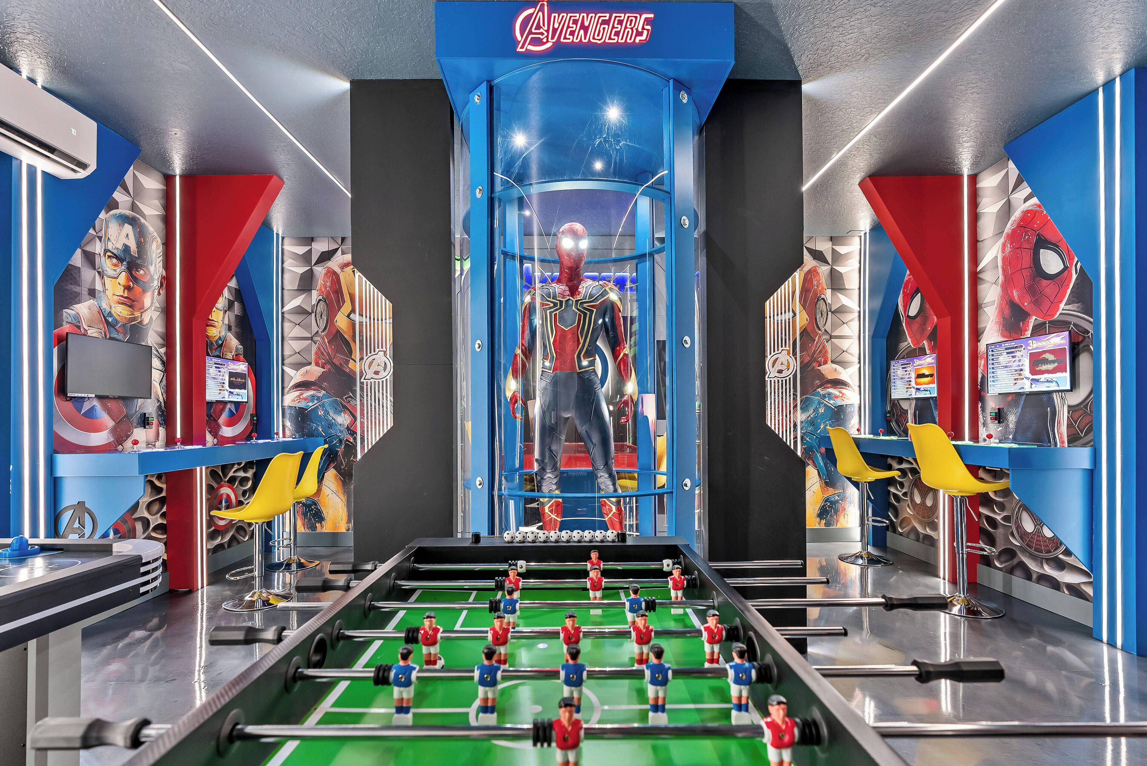 A room with a foosball table, a large window, and a Spider-Man themed wall.