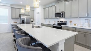 Cozinha moderna com uma ilha grande, eletrodomésticos de aço inoxidável e iluminação pendente.