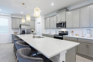 A modern kitchen with a large island, stainless steel appliances, and pendant lighting. - 9BR house sleeps 18 with spa and pool table (Kissimmee)