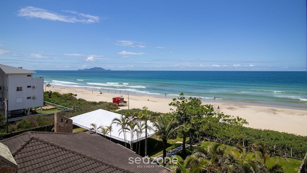 A beach view from a building with a tiled roof, a white building, and palm trees. - Apartment With BBQ in Condo With Pool Eaf0404 (Florianópolis)