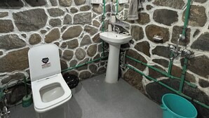 Un baño con pared de piedra, un lavabo blanco, un inodoro y un cubo verde.
