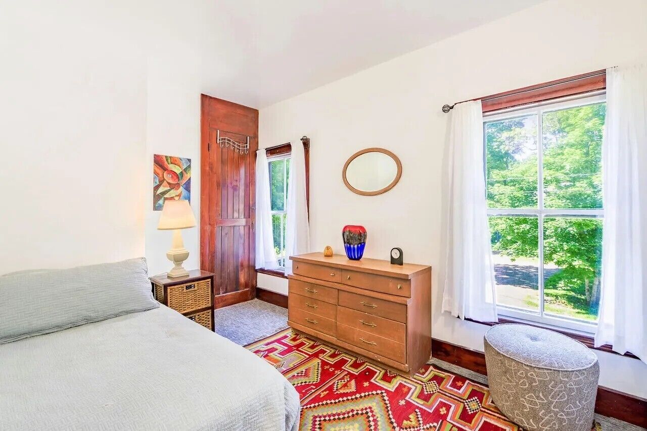 A bedroom with a bed, dresser, mirror, and a window with a view of greenery.