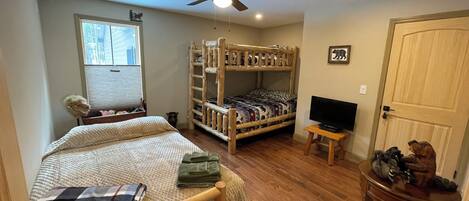 A bedroom with a bunk bed, a single bed, a ceiling fan, a TV on a small table, and a door with a dog figurine.