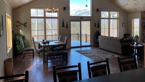 A spacious room with a high ceiling, wooden beams, a large dining table with chairs, a fireplace, and large windows offering a view of the outdoors. - Flying Goose - newly built 4-bedroom house with incredible views in Wilmington (Wilmington)