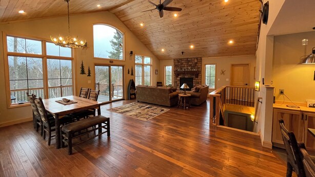 A spacious living area with a high ceiling, wooden floors, a fireplace, and large windows offering views of the outdoors. - Flying Goose - newly built 4-bedroom house with incredible views in Wilmington (Wilmington)
