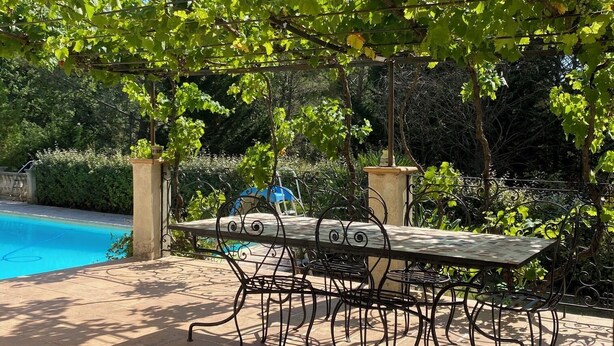 A patio with a table and chairs, surrounded by lush greenery and a swimming pool.