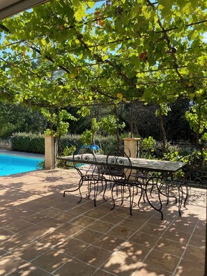 Un patio con mesa y sillas, rodeado de abundante vegetación y una piscina.