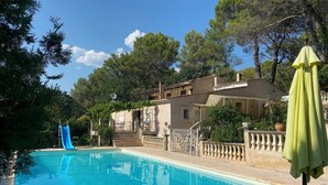 A swimming pool with a blue slide, surrounded by trees and a building with a balcony.