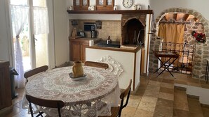A cozy kitchen with a stone fireplace, wooden cabinets, and a dining area with a lace tablecloth.