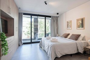 Ein modernes Schlafzimmer mit einem großen Bett, einem Flachbildfernseher und einer Glastür zum Balkon.