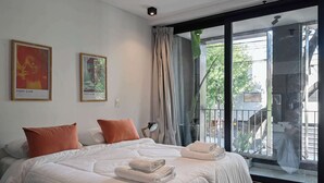 Une chambre d’hôtel avec un grand lit, deux oreillers, une table de chevet, une fenêtre avec des rideaux et deux affiches encadrées au mur.