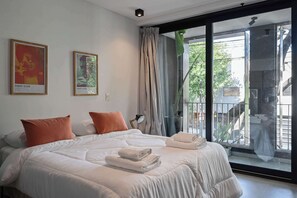 A hotel room with a large bed, two pillows, a nightstand, a window with curtains, and two framed posters on the wall. - MOT Rentals + Black Ravignani 1B - 3 pax Loft Palermo Hollywood (Buenos Aires)
