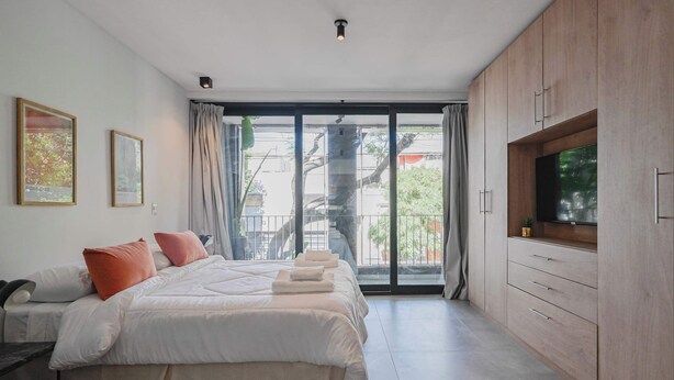Une chambre moderne avec un grand lit, une télévision et une porte-fenêtre coulissante donnant sur un balcon.