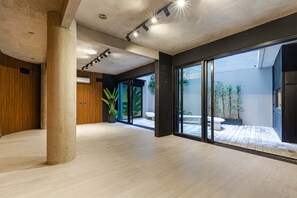 A spacious interior with a concrete pillar, a wooden wall, and a large sliding glass door leading to an outdoor area with plants. - MOT Rentals + Design SohoHaus '507' - 3 pax Full Amenities (Buenos Aires)