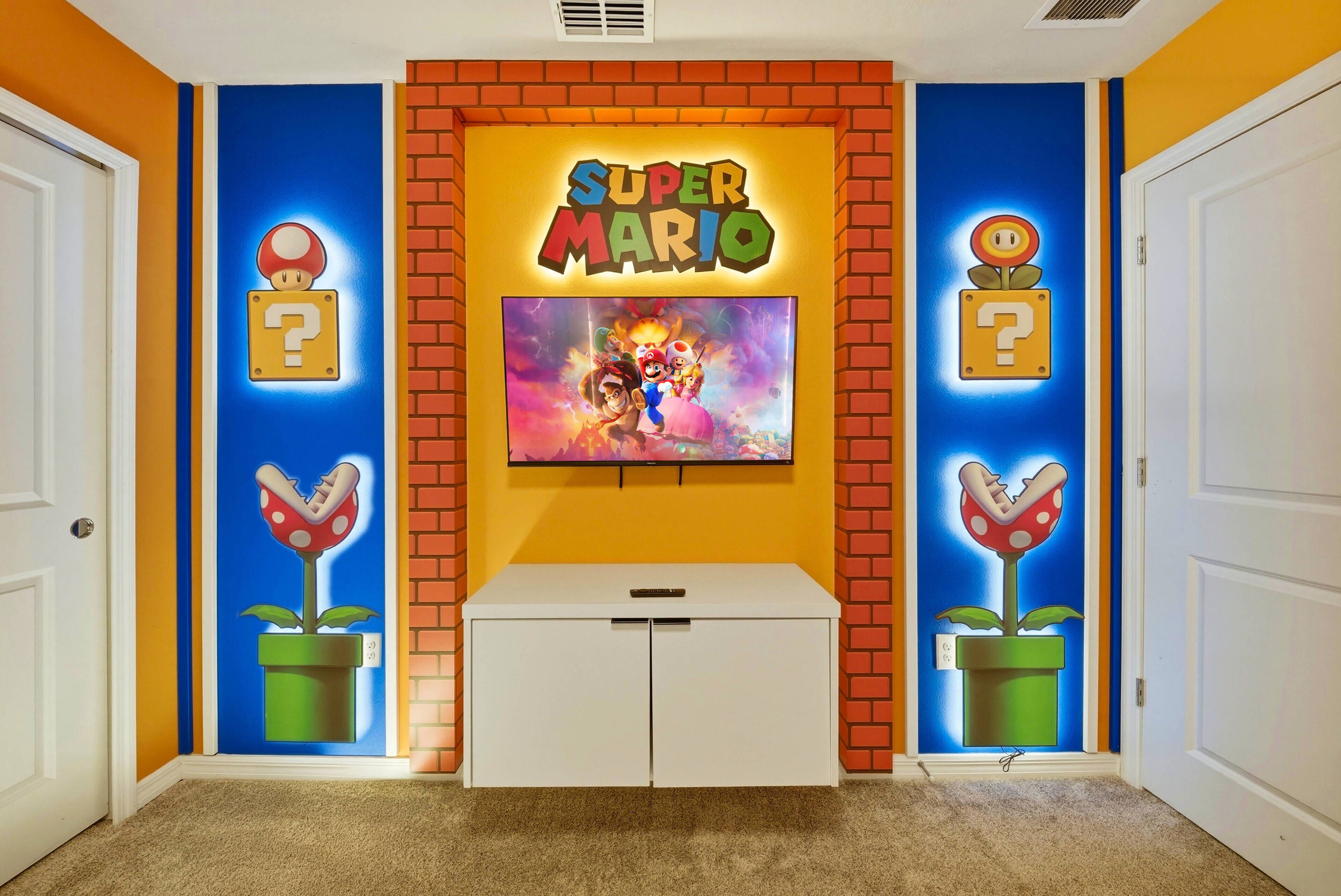Een hal met een muur in Super Mario-thema, een flatscreen-tv en een wit kastje.