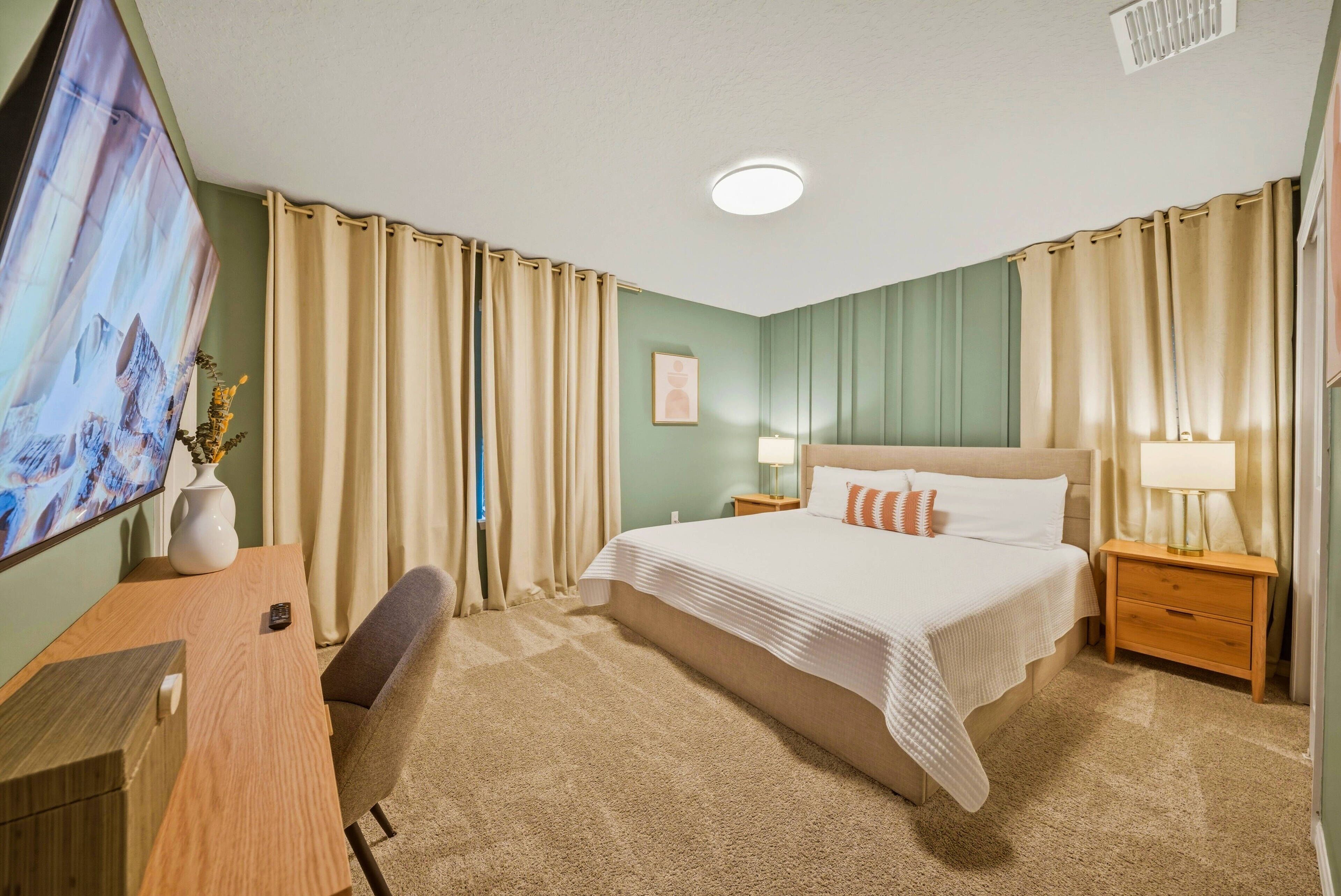 Et hotelværelse med seng, natborde, et skrivebord og et fjernsyn.