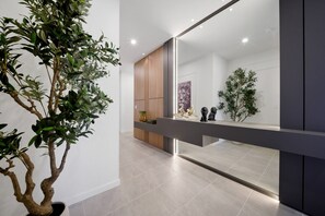 Ein modernes Interieur mit einem großen Spiegel, der einen Raum, einen Blumentopf und eine Holzkabine reflektiert.