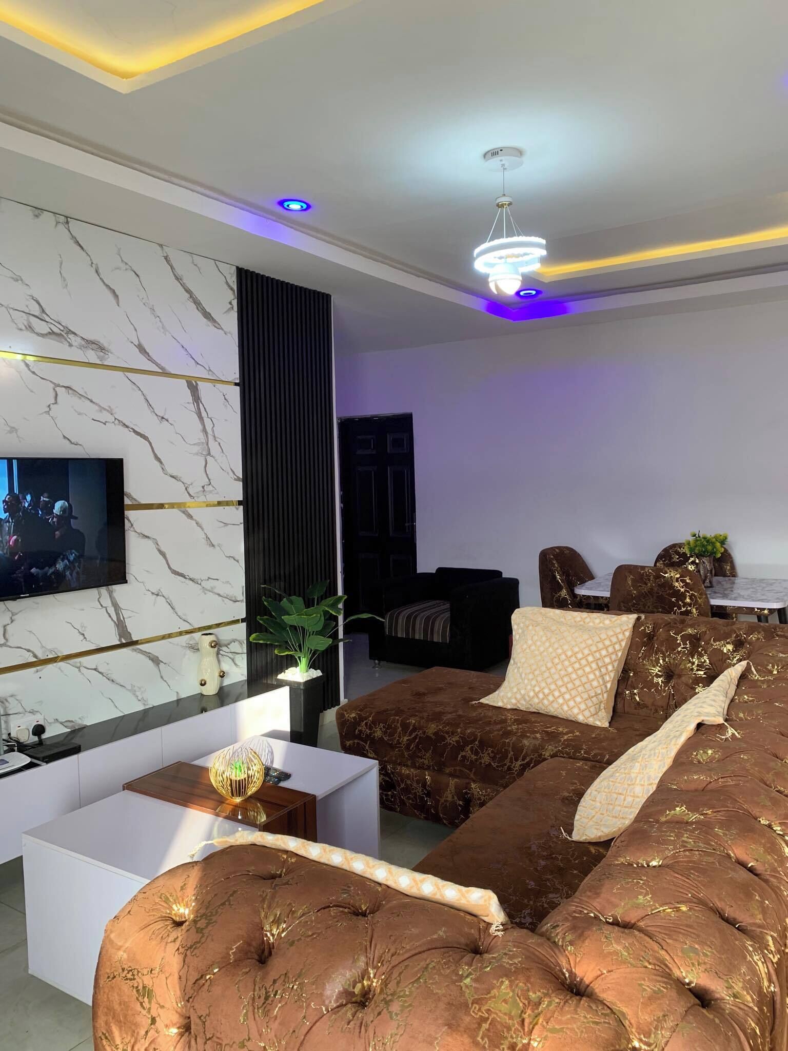 A modern living room with a marble wall, a large brown sofa, a coffee table, and a TV mounted on the wall.