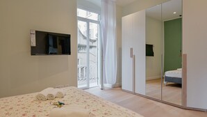 A bedroom with a bed, a wardrobe, a mirror, and a window with a view of buildings. - GuestHost - Cozy 59mq apartment, perfect for 4 people, located on the first floor of a building without a lift (stairs to access it).The property is located in a well-served residential neighborhood, adjacent to the Historic Center.The Central Station, r (La Spezia)