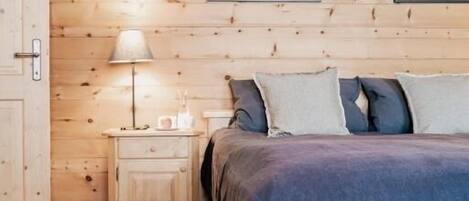 A wooden-paneled room with a bed, a nightstand, a lamp, and two framed pictures on the wall.