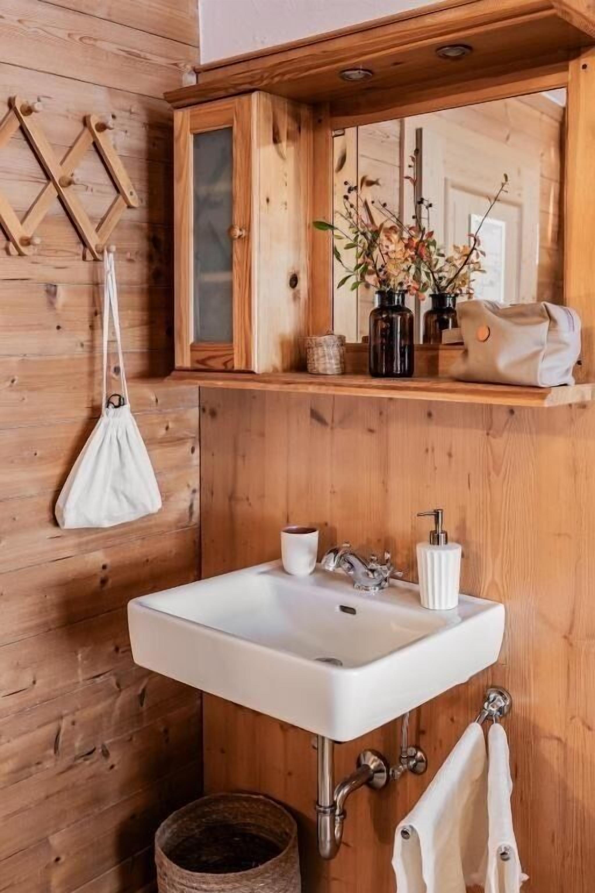 Un bagno in legno con un lavandino bianco, uno specchio e una borsa bianca appesa.