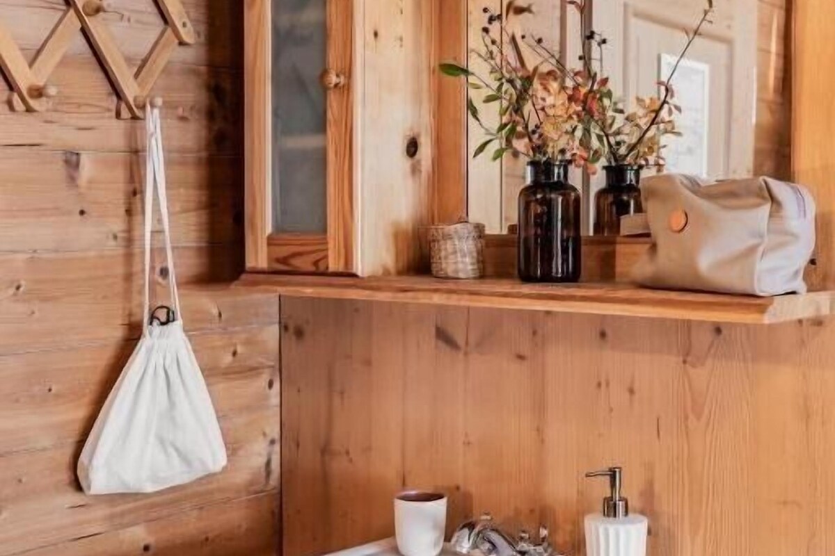 Un baño de madera con un lavabo blanco, un espejo y una bolsa blanca colgada.