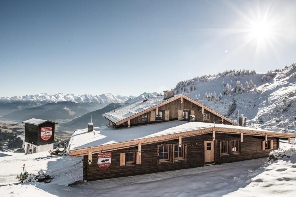 Una cabaña de madera en la montaña con techo inclinado, un cartel y vistas de montañas nevadas.