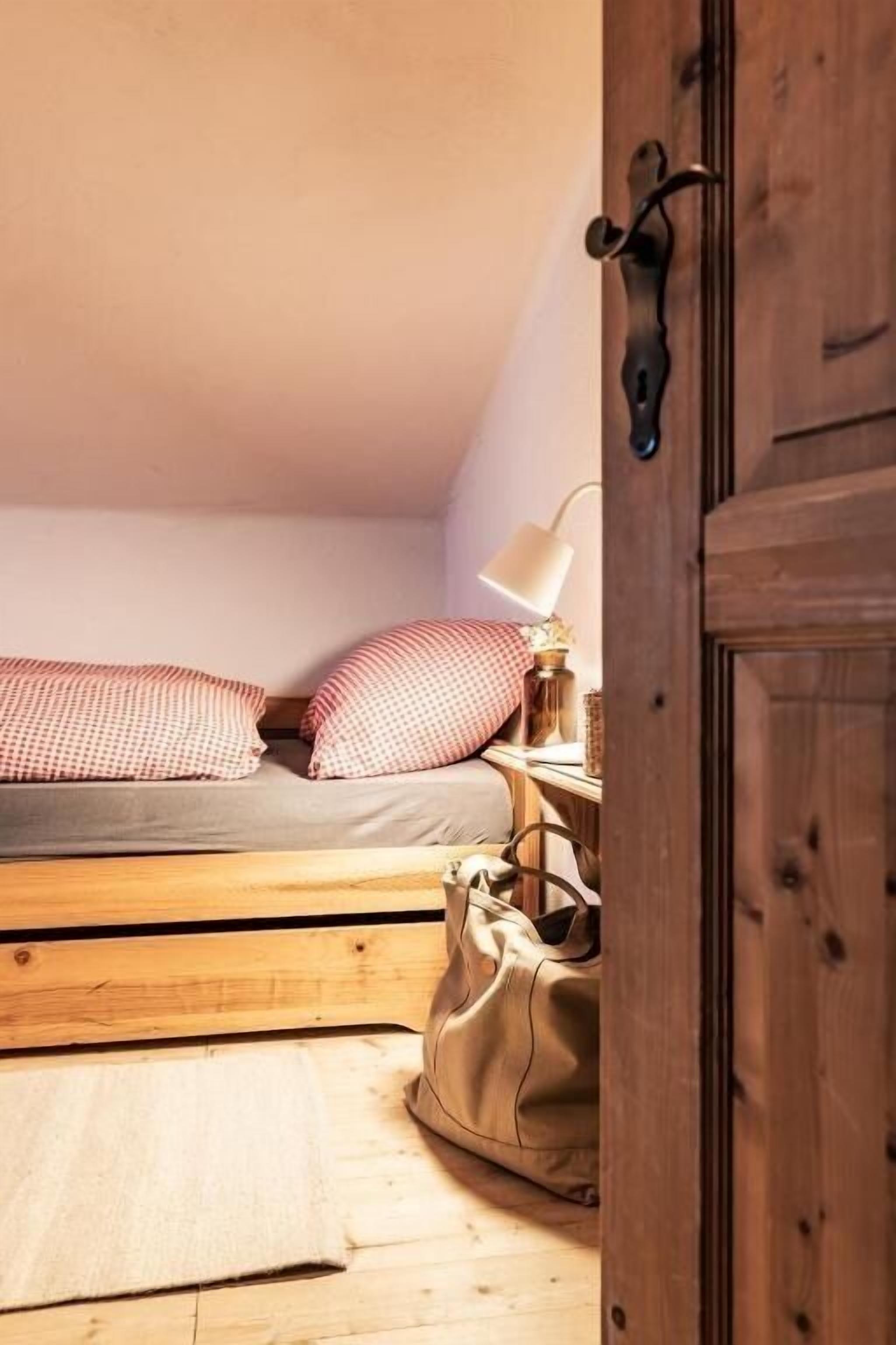Ein Schlafzimmer mit einem hölzernen Bett, einer Nachttischlampe, einer Tasche und einer Holztür.