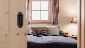 Een slaapkamer met een houten plafond, een raam met gordijnen, een bed met kussens en een nachtkastje met een lamp.